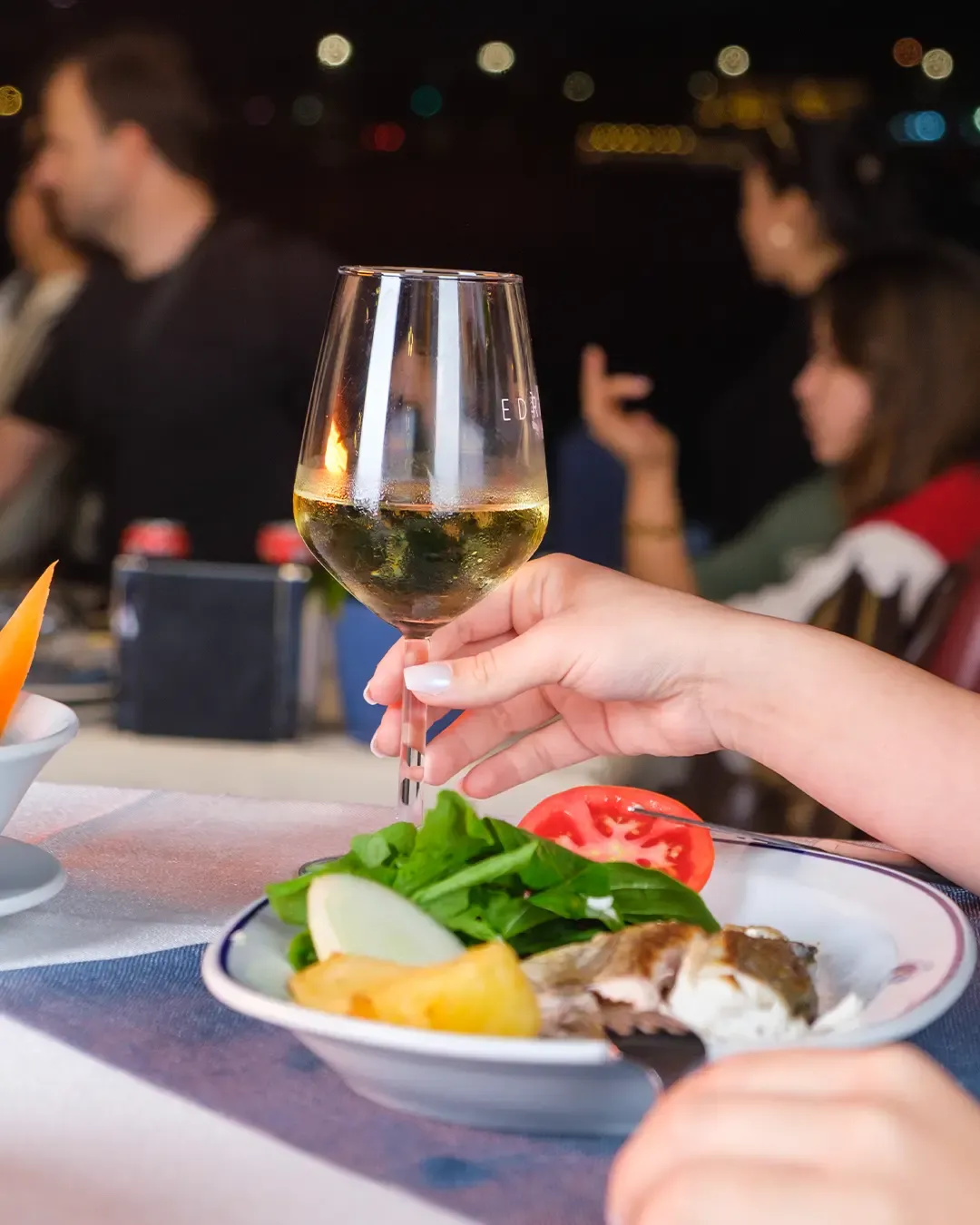 A glass of white wine and a plate of grilled fish at an evening table
