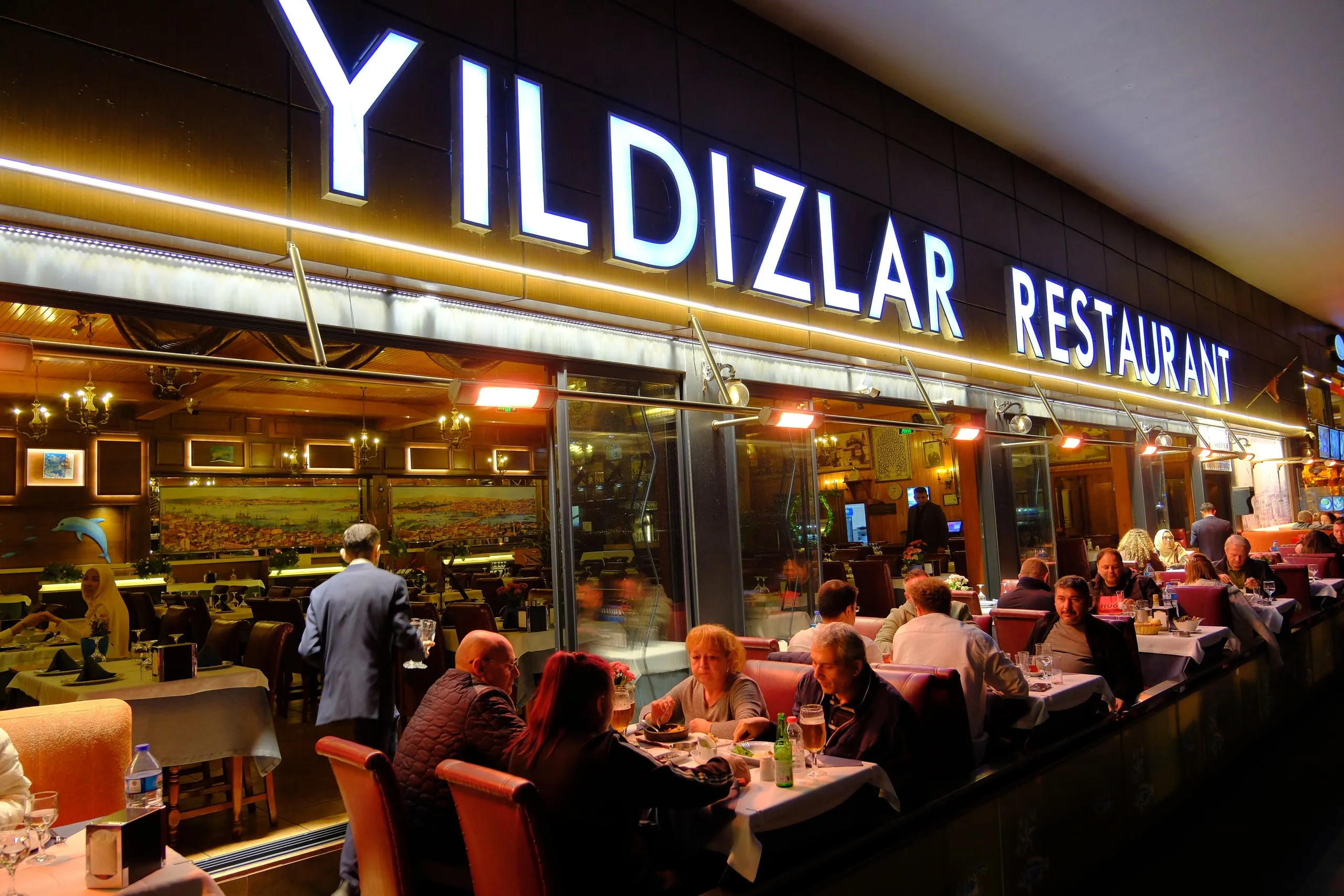 Yıldızlar Restaurant’s illuminated sign and busy tables beneath the Galata Bridge